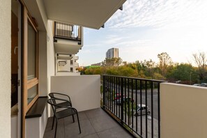 A view of the balcony, furnished with chairs and a table. Greenery and buildings can be seen in the distance.