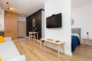 A TV mounted on the wall, facing the gray sofa. The room is spacious with wooden flooring.