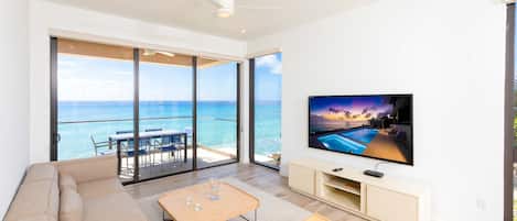 Living area with television, elevated ocean views, and a walkout furnished balcony. 