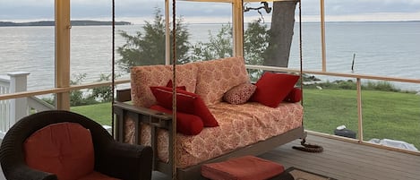 Swinging daybed, cushioned outdoor furniture set on screen porch. 