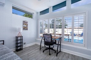 A room with a desk, and a desk chair. It features an air conditioner and plenty of natural light 