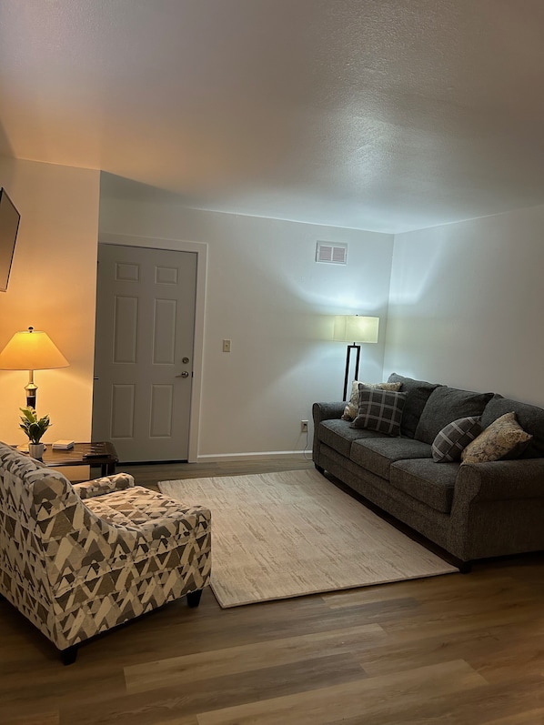 Living room with sofa, chair, area rug, end table, lamps and tv.