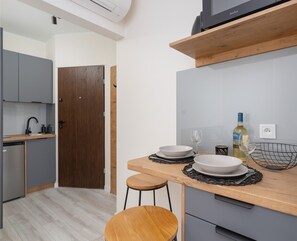 A compact dining area with a round table, wooden chairs, and a stylish kitchenette in the background.
