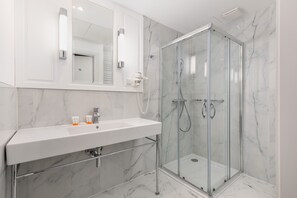 A luxurious bathroom with marble walls, a walk-in shower, and polished fixtures.
