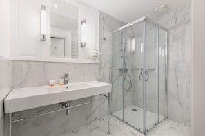 A luxurious bathroom with marble walls, a walk-in shower, and polished fixtures.