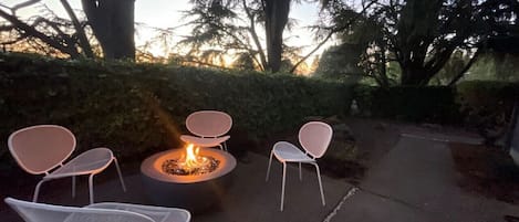 Gather 'round the warmth and beauty of a fire pit, nestled amidst nature's embrace. This inviting scene features ample seating for a cozy group of friends or family, with comfortable chairs and rustic wooden benches encircling the flickering flames.