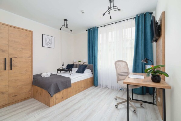 A modern bedroom with wooden furniture, gray bedding, and a workspace by the window.
