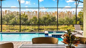 Screened-in pool with spa, forest views, and serene outdoor dining space.