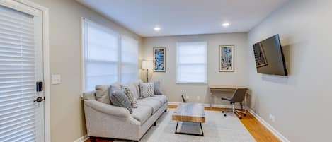 Living room with couch, coffee table writing desk and chair, lamp and 55” TV