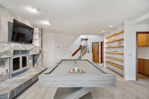 On the lower level is a family room: 9 foot pool table, bar cart + refrigerator, and pub table. Just outside this family room is an outdoor bar area and the pool beyond.