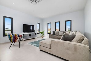 The living room area features a large sofa set, A large TV, and an eye-catching, colorful chair with armrest knot tweed.