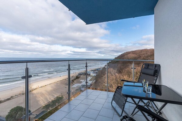 A balcony with a breathtaking view of the sea and cliffs, furnished with a small table and chairs.
