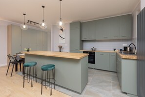 A spacious kitchen with green cabinetry, an island with bar stools, and pendant lighting.
