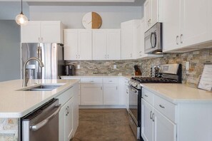 The kitchen is highlighted by a neutral color scheme and a spacious surrounding floor plan. It is fully equipped with all necessary appliances, utensils, and storage for bounteous cooking preparation.