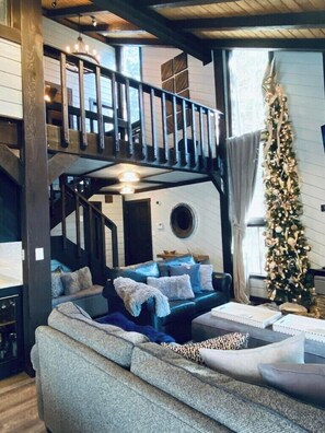Marvel at the spacious and inviting living area featuring high vaulted ceilings, a stylish loft, and ample seating. The beautifully decorated Christmas tree and rustic decor create a warm, festive atmosphere.