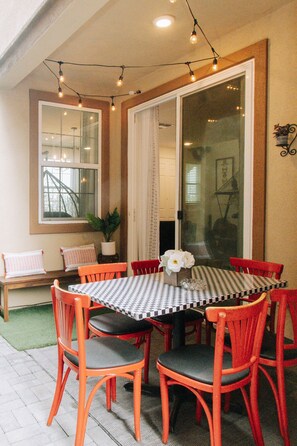 Covered outdoor patio with string lights, dining area and BBQ.