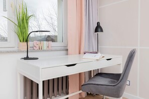 A bright home office featuring a white desk, gray chair, and a large window for natural light.
