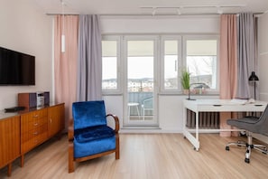 A stylish living room with a blue armchair, wooden sideboard, and large windows.
