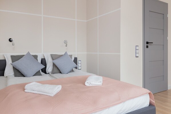 A cozy bedroom with pastel bedding, decorative pillows, and bright, modern lighting.
