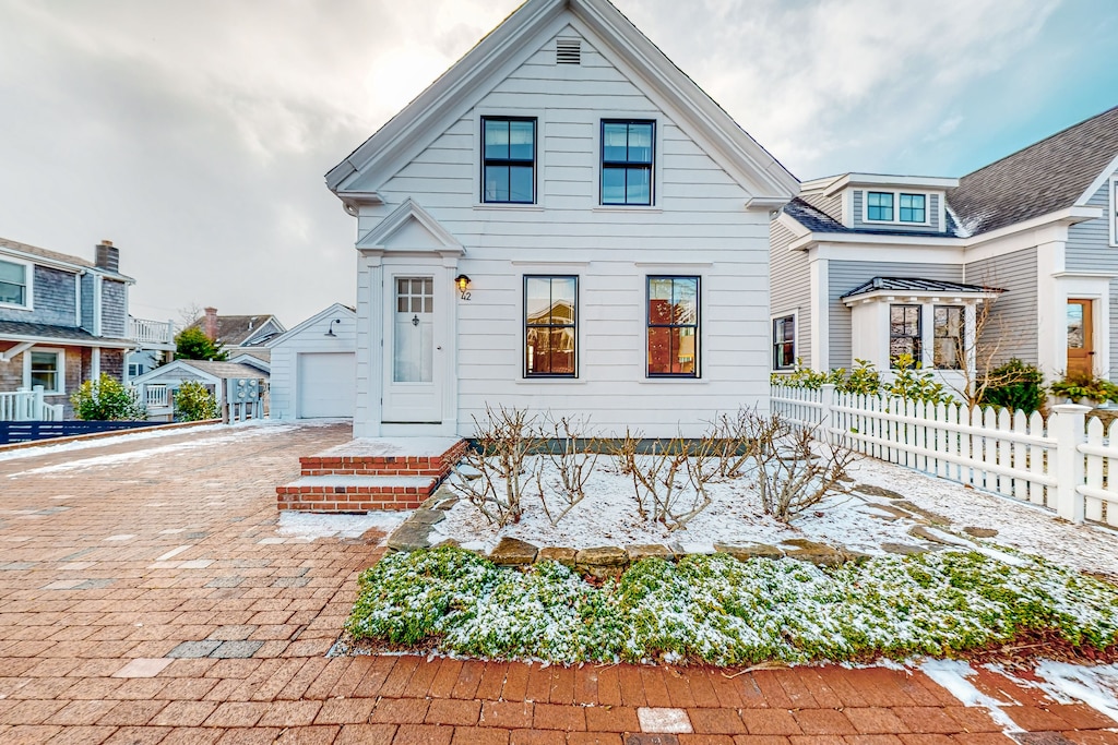 A white two story historic home sits in a neighborhood of Provincetown with red brick streets and a cloudy sky overhead