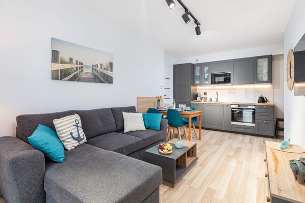 A cozy living room with a gray sofa, turquoise accents, and a kitchenette in the background.

