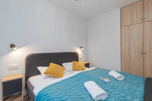 A bright bedroom with two single beds, a wardrobe, and vibrant turquoise bedding.
