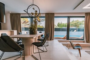 Ein Blick auf den eleganten Essbereich im minimalistischen Design mit Tisch und Stuhl, ein interessanter Kronleuchter mit Blick auf den Pool sind in einer neu gebauten dalmatinischen Ferienvilla zu vermieten in der Nähe von Sibenik