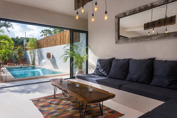 Living room with a modern design and comfortable sofas. Large windows connect to the outside and provide a beautiful view of the pool.