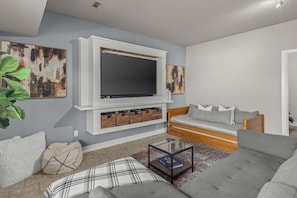 The Living room showcases a wall-mounted TV with storage below, surrounded by abstract artwork and cozy seating options. With a soft color scheme and modern furniture, including a comfortable gray sofa, a patterned bean bag, and a sleek glass coffee