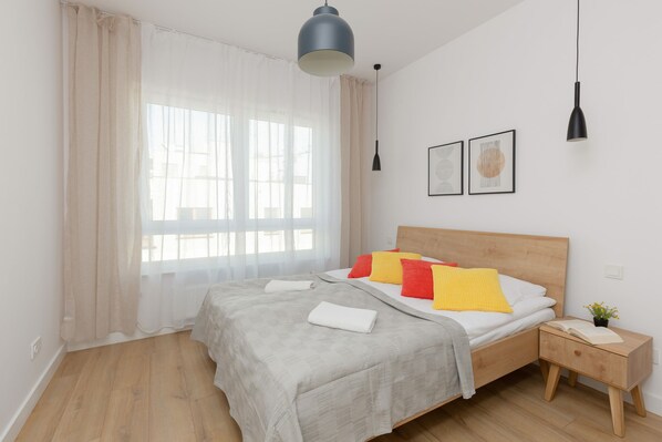 A cozy bedroom with a double bed, gray bedding, and bright natural light from large windows.