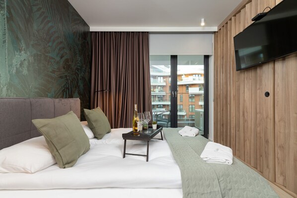 A stylish bedroom with a large bed, green bedding, and a wall-mounted TV, complemented by warm wooden accents.
