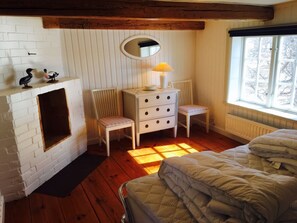 Sovrum nr 3,  övervåning med dubbelsäng och liten öppen spis. Här i morgonsol med utsikt över sjön och herrgårdens park med blodbokar och lindar.