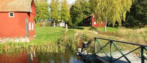 Utsikt från bryggan mot huset till höger, till vänster en gammal bak och tvättstuga, där även bastun finns. I bakgrunden skymtar gaveln på herrgården.