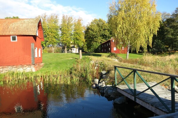 Utsikt från bryggan mot huset till höger, till vänster en gammal bak och tvättstuga, där även bastun finns. I bakgrunden skymtar gaveln på herrgården.
