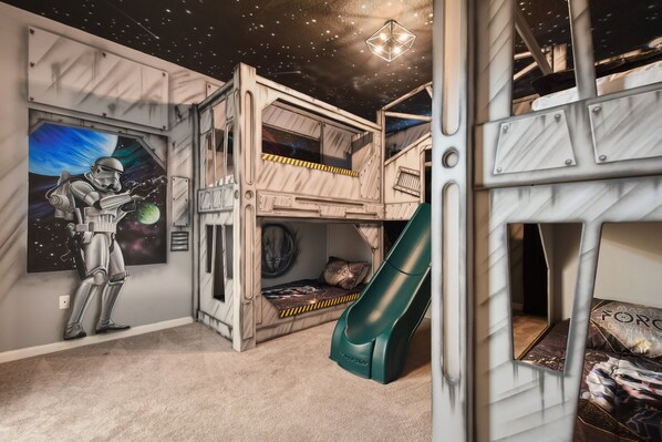 Space-themed kids' bedroom with bunk beds, slide, galaxy murals, and cosmic vibes.