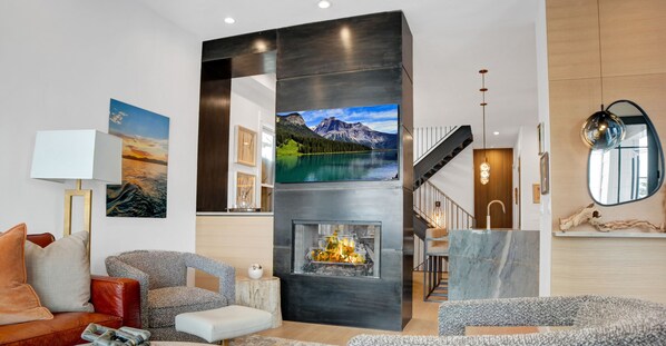 An artistically designed black fireplace mantel with mounted flat screen TV, grey club chair and footrest.