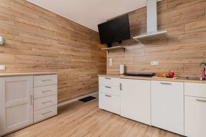 A compact kitchen with white cabinets, wooden accents, and a wall-mounted TV.
