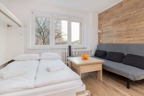 A bright bedroom with a double bed, white bedding, and a sofa for added comfort.

