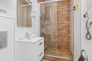 A modern bathroom with a walk-in shower, white tiles, and a sleek design.
