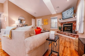 Warm and inviting living room with cozy seating, a rustic brick fireplace, and a charming bicycle-themed decor accent.