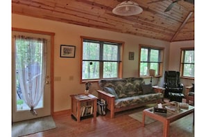 Living area has a coffered pine ceiling w/fan, & large windows with wooded views