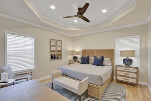 Primary King Suite with Tray Ceiling – Mallery Beach House - The main suite delivers peace and polish, with a king bed, tray ceiling, warm wood accents, and natural light. It’s the kind of room that makes sleeping in feel earned.