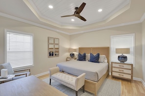 Primary King Suite with Tray Ceiling – Mallery Beach House - The main suite delivers peace and polish, with a king bed, tray ceiling, warm wood accents, and natural light. It’s the kind of room that makes sleeping in feel earned.