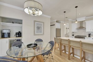 Dining Room and Coffee Station – Mallery Beach House - This is where mornings start and evenings wind down. With a round glass-top table, bar seating, and a fully stocked coffee bar—including a premium filtered water tap built into the cabinet—everything here is built for real-life comfort that doesn’t skip the details.