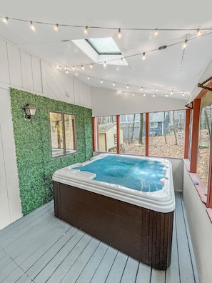 Huge 6 person hot tub in screened porch w/ string lights.