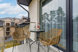 A balcony with chairs and a table, overlooking greenery and modern buildings.
