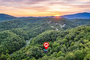 In this drone photo from high above the Smoky Mountains, the Grillin Bear Lodge nestles peacefully among lush trees, framed by a breathtaking sunset- a hidden gem in nature's paradise.