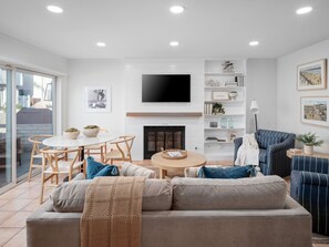 This cozy and light-filled living space features contemporary seating, calming décor, a fireplace, a dining area, and a Smart TV.