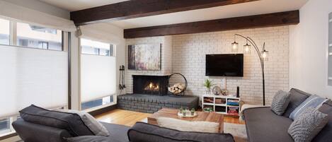 Spacious living room with wood-burning fireplace (photo shows privacy blind). Couches convert into two twin-sized beds.