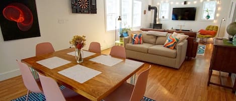 Dining area and living room with two couches, electronic dart board, smart TV and speakers, wood stove, and a closet full of board games